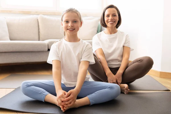 穿着运动服的积极的千年期高加索妇女和十几岁的女儿练习瑜伽 在客厅室内的垫子上训练 家庭体育 身体护理和保健一起进行 — 图库照片