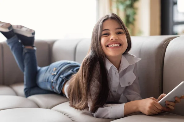 移动报价 快乐的未成年少女在家里用电话和微笑拍摄沙发上的照片 儿童滚动社交媒体 在手机上参与在线娱乐 儿童和小工具 — 图库照片