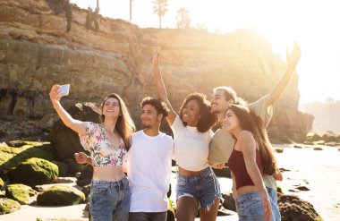 Binlerce yıllık neşeli uluslararası insanlar yaz tatilinin tadını çıkarıyorlar, eğleniyorlar, sahilde akıllı telefondan selfie çekiyorlar. Blog için fotoğraf, sosyal ağ, uygulama, yaşam tarzı ve birlikte hafta sonu