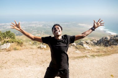 Eğitimden ve okyanus manzarasından zevk alan heyecanlı siyahi adam, sabah egzersizinden esinlenerek iki elini kaldırıyor. Spor ve sağlıklı bir yaşam tarzı.