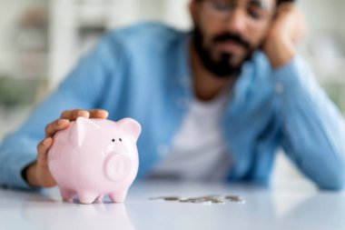 Finansal kriz. Üzüntülü Hintli adam domuz kumbarasından alınan paraları sayıyor, Depresyondaki Doğulu adam para sıkıntısı çekiyor, Bütçe planlamada zorluk yaşıyor, domuz kumbarasına odaklanıyor,