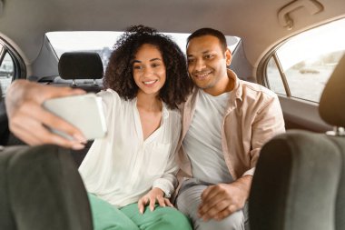 Aktar. Mutlu bir orta doğu çifti cep telefonuyla selfie çekiyor, arka koltukta oturuyor ve taksi sürerken eğleniyor. Eşler otomobille yaz yolculuğunun keyfini çıkarırken, ön koltuktan manzara