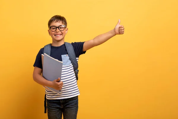 快乐快乐的高加索男孩学生背着背包 手里拿着书 露出大拇指和微笑 孤立在黄色的背景下 复制空间 对学生来说是个好机会 — 图库照片