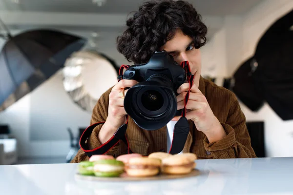 stock image Food photographer caucasian man taking photos of delicious sweets macarons at photo studio, using digital camera and professional lighting equipment