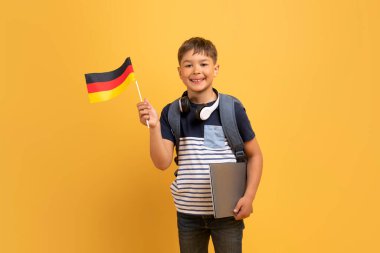 Yurtdışındaki çocuklar için eğitim, yabancı diller okulcular için öğrenme kavramı. Sırt çantalı, elinde Alman bayrağı olan, sarı arka planlı, neşeli, yakışıklı, beyaz okul çocuğu.