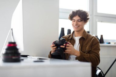 Modern sanatlar ve yaratıcı kariyer kavramı. Mutlu gülümseyen fotoğrafçı elinde kamerayla stüdyoda iş yerinde oturuyor.