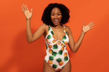 Tatil, yaz tatili, seyahat. Duygusal olarak mutlu, gür saçlı, ananaslı, turuncu arka planda izole edilmiş güzel siyah bir kadın.