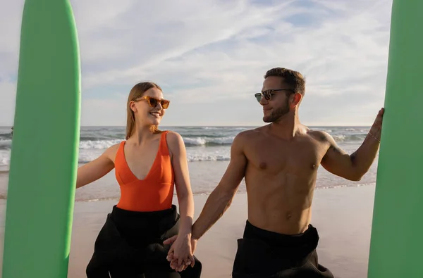美しい若いサーファーのカップルの肖像画ビーチにポーズをとっているサーフボード スタイリッシュなサングラスを手にして一緒にサーフィンしながら楽しむ幸せな恋人たち — ストック写真