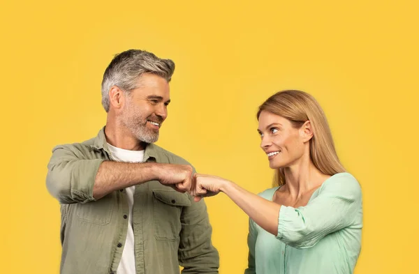 stock image Teamwork concept. Happy middle aged man and woman bumping fists and smiling, celebrating success partnership triumph standing on yellow studio background