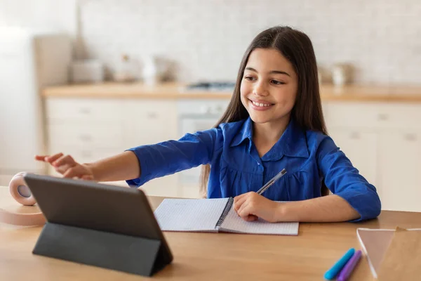 家教教育 积极的十几岁以下的女孩使用数字平板电脑 在笔记本上写作业 坐在现代家庭内部的桌旁 小学生通过平板电脑学习冲浪网 — 图库照片