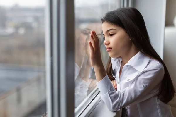 Preteen Depression. Side View Of Sad Little Girl Looking Outdoors Standing And Touching Window At Home, Feeling Lonely And Depressed Indoor. Child Mental Health Problem Concept
