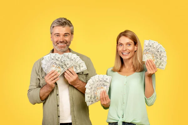 家庭储蓄概念 快乐的中年夫妇孤零零地站在黄色的工作室背景上 露出钞票 看着相机 — 图库照片