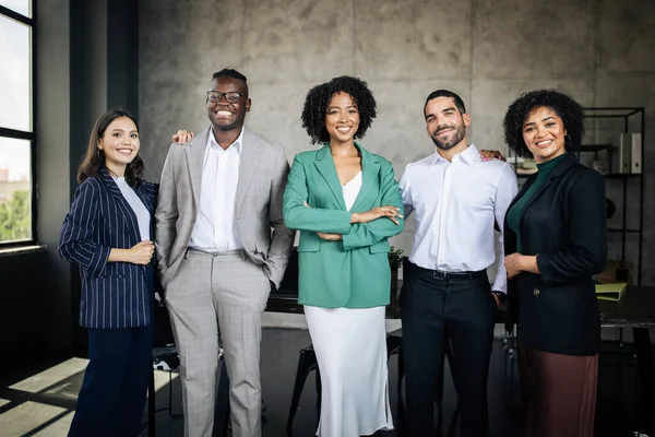 International Business Team. Five Multiethnic Businessmen And Businesswomen Coworkers Posing Standing In Modern Office Indoor, Smiling At Camera. Colleagues Expressing Confidence In Career Success
