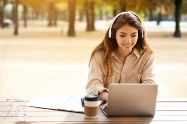 Online Öğrenme Teklifi. Kulaklıklı mutlu İspanyol öğrenci kadın dışarıda dizüstü bilgisayarda çalışıyor, üniversite kampüsü parkındaki masada oturmuş eğitici internet konferanslarını izliyor. Boş boşluk