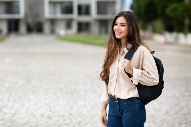 Üniversite Eğitimi. Üniversitede açık havada poz veren, sırt çantalı ve boş alana bakan, günlük giysiler giyen mutlu Latin öğrenci kadın. Modern çalışma, bilgi kavramı