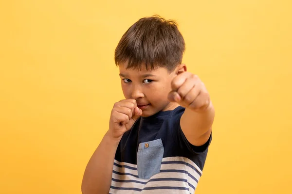 子供のための芸術 黄色の背景に彼の拳を示すかわいいスポーティな白人の男の子の年齢の子供の閉鎖スタジオショット カメラで空手キックを実証 — ストック写真
