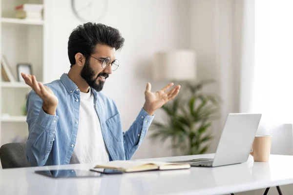 Stressed Young Indian Freelancer Man Suffering Problems While Working With Laptop At Home Office, Confused Eastern Guy Looking At Computer Screen And Raising Hands In Shock, Free Space