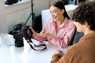 Çekimden sonra fotoğraf çeken mutlu kadın fotoğrafçı, stüdyodaki adamla iş tartışan, fotoşoptan sonra konuşan ve en iyi resimleri seçen, iş yerinde oturan.