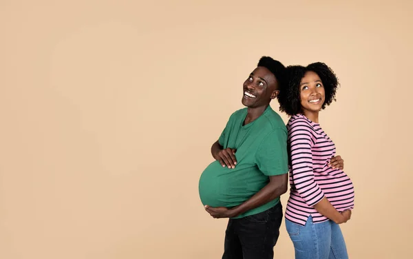カジュアルな雰囲気の中で大きな腹を持つ幸せな若いアフリカ系アメリカ人の夫と妊娠中の妻が一緒に楽しみ ベージュのスタジオの背景に隔離された赤ちゃんを待ってお楽しみください 愛と家庭と関係 — ストック写真