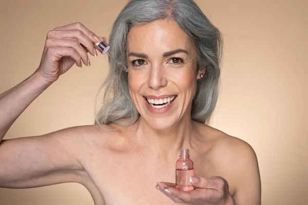 Glad Sensual Mujer Mayor Sosteniendo Botella Con Producto Belleza Aplicando — Foto de Stock