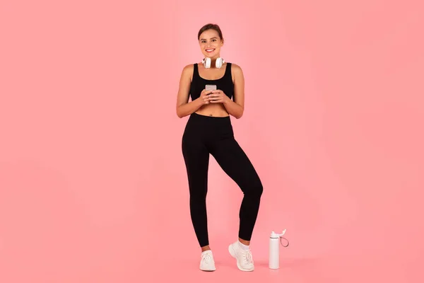 Happy Young Sporty Woman Activewearusing Smartphone While Standing Pink Studio — Stockfoto