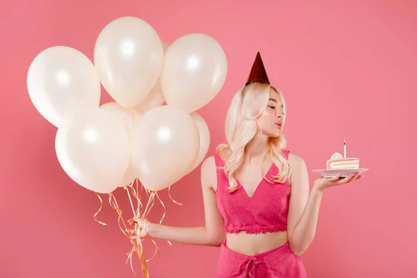 かわいいですヨーロッパの女性風船がケーキの上にキャンドルを吹いて ピンクのスタジオの背景の上にポーズ 彼女の誕生日を祝う 休日パーティーを持っている — ストック写真
