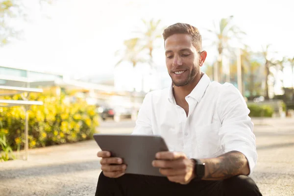 陽気な髭のビジネスマンは 休憩中にオフィスの近くに屋外に座って デジタルタブレットでニュースを読んで 上司はビジネス戦略を計画し 新しい通常とアプリ — ストック写真