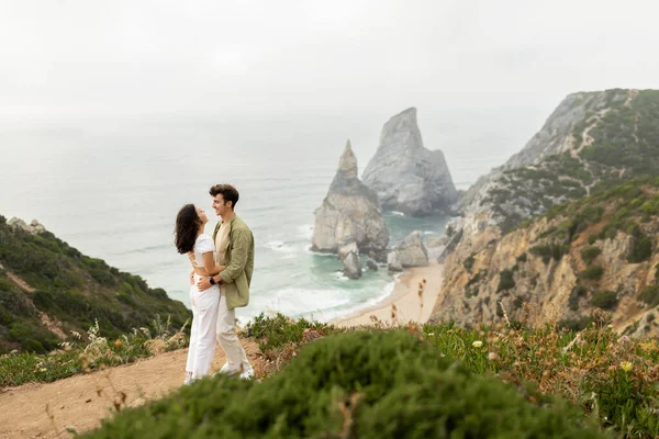 恋爱中的年轻夫妇有着浪漫的约会 拥抱在一起 站在海边的岩石悬崖上 在海岸线上尽收眼底 尽享悠闲的空间 — 图库照片