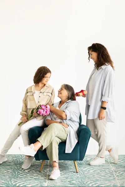 快乐的欧洲成年人和青少年女性送给老奶奶一束鲜花 坐在扶手椅上 隔离在白墙的背景下 工作室 母亲节 — 图库照片