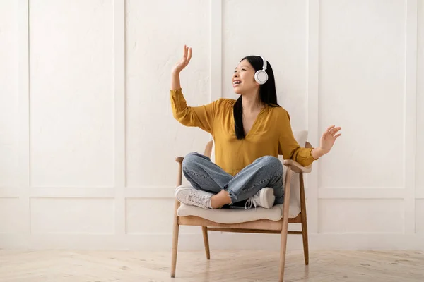 ストレス解消 自宅でのリラクゼーション 楽しい幸せな若いアジアの女性は アームチェアに座って ワイヤレスヘッドフォンを使用して 閉じた目で音楽を聞いて 歌と踊り コピースペース — ストック写真
