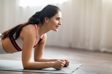 Yakından bakınca mutlu, esmer, spor kıyafetli, spor kıyafetli genç bir kadının yoga minderini ören sportif bir bayanın fitness reklamı için fotokopi odasına baktığını görüyoruz.