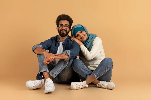 ロマンチックな笑顔のイスラム教徒のカップルの肖像画ベージュスタジオの背景に座って 陽気なアラブの配偶者 男と女でハイジャブ抱擁し カメラを見て 幸せなイスラム家族の抱擁 コピースペース — ストック写真