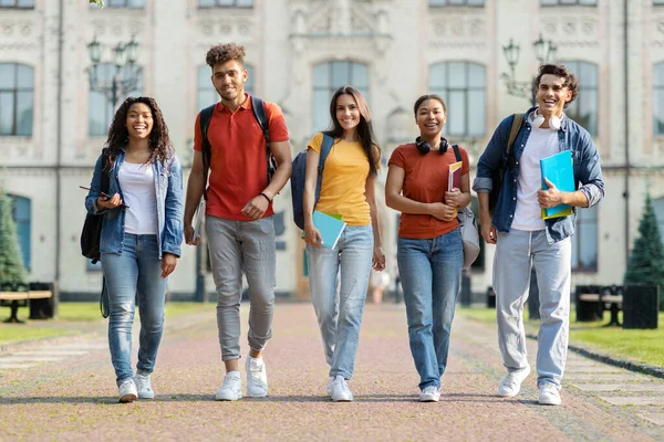 快乐的大学生们一起在校园里散步 快乐的多民族大学生朋友们背着背包和练习本 笑着看着相机 呆在户外 长篇大论 — 图库照片