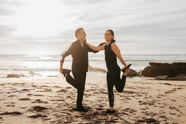 在早上和室外的海滩上 笑着穿运动服的资深高加索夫妇伸展腿 练习瑜伽 享受锻炼和积极的生活方式 一起运动 — 图库照片