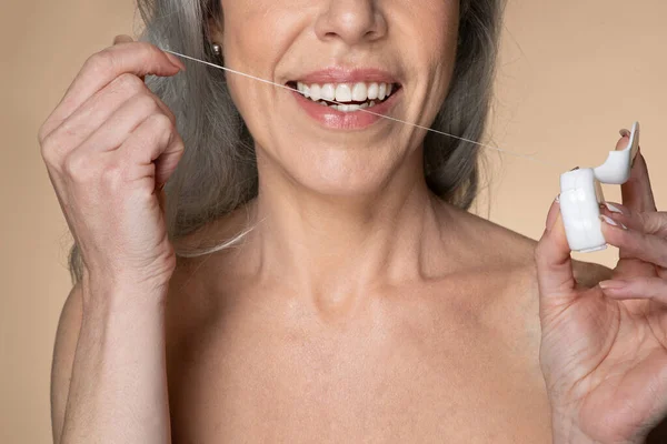 歯のケアと口腔治療 閉鎖クロップドビューの認識できないシニア白髪の女性を使用して歯科フロス 朝ルーチンを行います ベージュの背景 — ストック写真