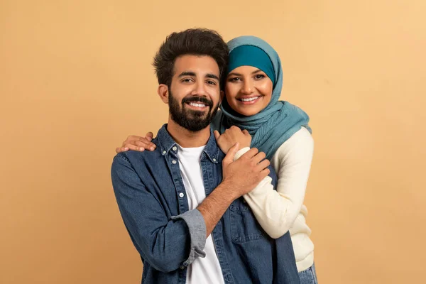 Retrato Feliz Pareja Musulmana Joven Abrazando Sobre Fondo Beige Sonriendo —  Fotos de Stock