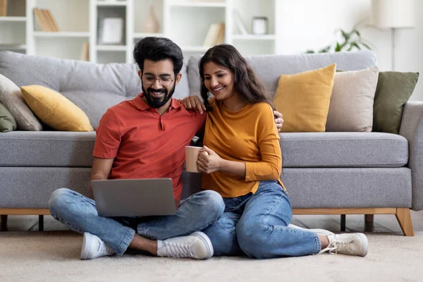 国内パスタイム 幸せな若いインド人の配偶者が自宅でノートパソコンで休憩し リビングルームで床にくつろぎ インターネットを閲覧し コーヒーを飲みながら 無料のスペース — ストック写真