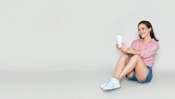 夏の服を着たかわいい陽気な幸せなかなり若い女性は コピースペースのパノラマ 自撮りを取り スマートフォンを使用して パステルカラーの背景に隔離された床に座っています ソーシャルメディア ブログ — ストック写真