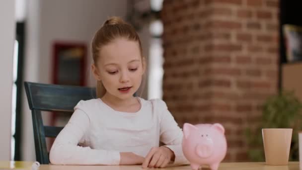 儿童金融知识普及 可爱的小女孩把硬币放进储蓄罐 在家里拍手 享受着她的第一笔积蓄 跟踪镜头 自由自在 — 图库视频影像