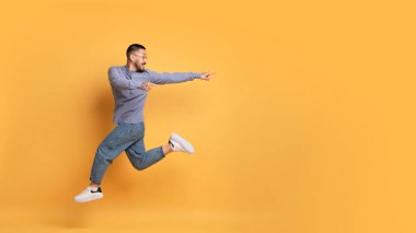 Harika bir teklif. Pozitif Asyalı adam havaya sıçrıyor ve sarı arka plandaki fotokopi alanını işaret ediyor. Neşeli, yakışıklı, milenyum adamı reklam ve panorama için bedava yer gösteriyor.