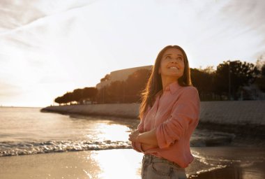 Gün batımında sahilde dikilen güzel orta yaşlı kadın, gülümseyen olgun kadın açık deniz kenarında dinleniyor, rüya gibi kadın yaz tatilinden ve tatilden keyif alıyor, kopyalama boşluğu.