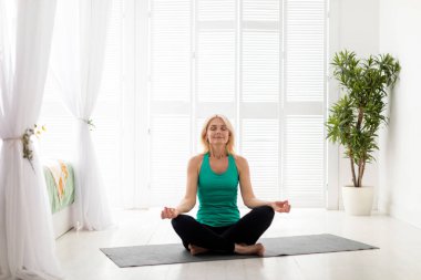 Sabah meditasyonu. Evde meditasyon yapan sakin, yaşlı bir kadının portresi. Nilüfer pozisyonunda oturan, gözleri kapalı rahat bir kadın. Açık oturma odasında yoga yapıyor.