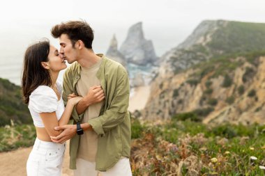 Sahilde kucaklaşan ve kaynaşan romantik çift, okyanus kıyısındaki kayalıklarda buluşuyorlar, sevecen erkek ve kadın birlikte sarılıyor ve eğleniyorlar, boşluğu kopyalıyorlar.