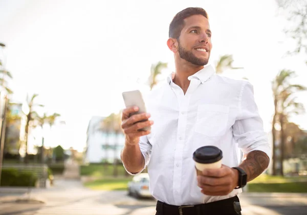 コピースペースを脇に見て 休憩を楽しんで 携帯電話を使用して移動し コーヒーを飲んで 街を歩く正式な服装で陽気な若い男起業家 — ストック写真