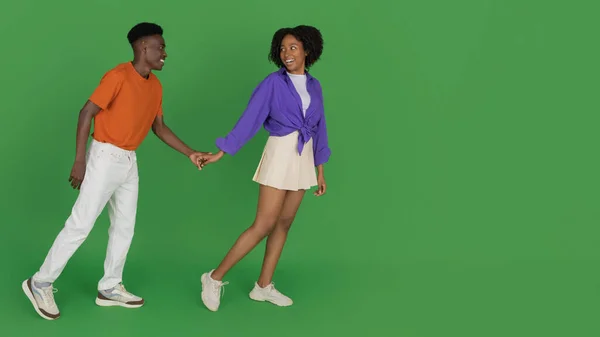 カジュアルなホールドボーイフレンドの手で若いアフリカ系アメリカ人女性の笑顔 リード 緑のスタジオの背景に隔離され 完全な長さ パノラマ 一緒に歩く ロマンチックなデート 広告とオファー — ストック写真