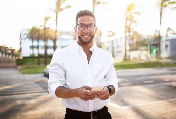 幸せな若いヨーロッパの男性起業家は 屋外で休憩中に電子メールをチェックし 携帯電話やカメラで笑顔を使用しています 電話を持つ陽気な白人ビジネスマン — ストック写真