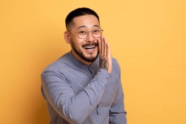 Yakışıklı Asyalı Adam Ağız Yakınında, Haberleri ya da Kameradaki Dedikoduları Paylaşan, Sarı Stüdyo Arkaplanı 'nda İzole Edilmiş, Yakın plan Çekimi, Boşluk Kopyalama