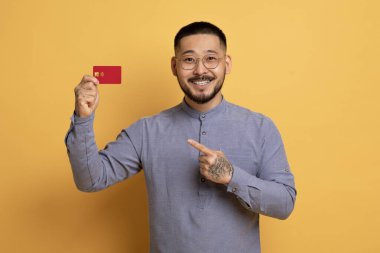 Elinde kredi kartı olan ve kameraya bakan neşeli Asyalı genç adam, sarı stüdyonun arka planında dururken mutlu bir milenyum adamının banka hizmetlerini önermesi, boşluğu kopyalaması...