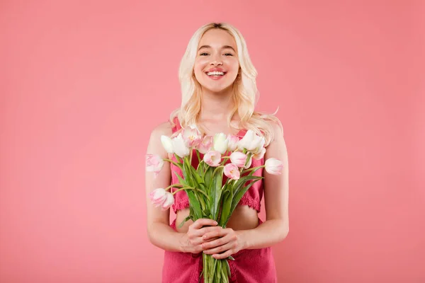 花の花束を保持幸せな魅力的なブロンドの女性は ピンクのスタジオの背景にポーズをカメラで笑顔 女性の日や誕生日をお楽しみください 人間の感情おめでとう — ストック写真