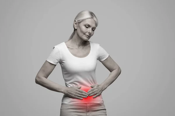 胃の痛みを持つ病気の成熟した女性 赤い炎症を起こしたゾーンで彼女の腹部に触れます 胃腸疾患に苦しんでいるシニア女性 スタジオの背景にポーズ 黒と白の写真 — ストック写真